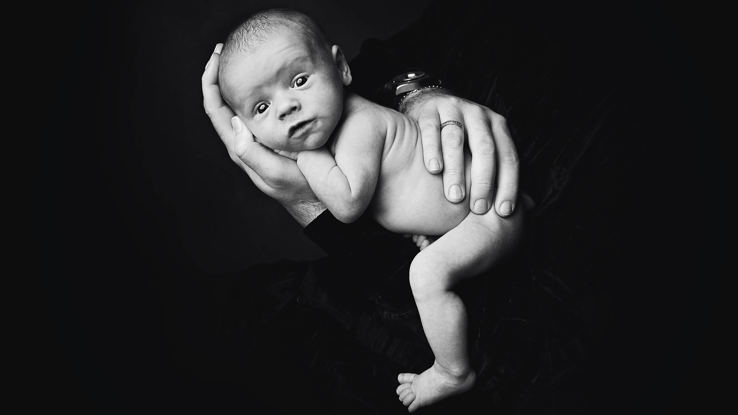 Striking black and white photo of a newborn baby in Dads arms at a shoot with AnA Photography