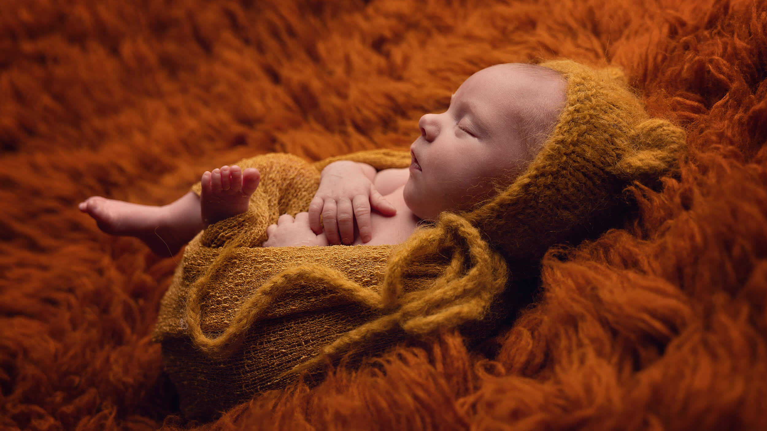 Newborn baby on orange fluff at a baby photo shoot in Cornwall with AnA Photography