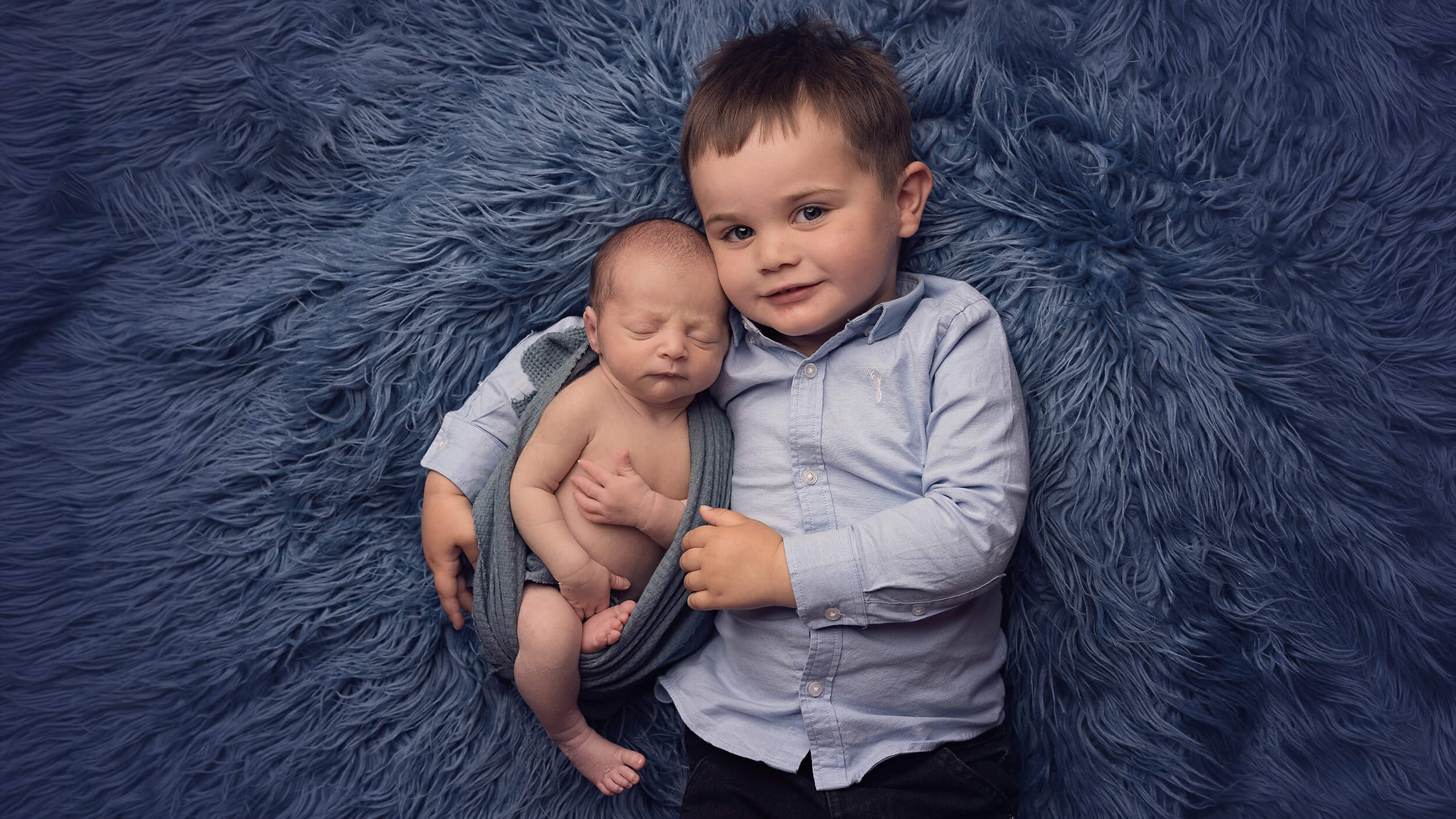 A young boy with his newborn baby brother, cuddling for a photo at AnA Photography in Cornwall.