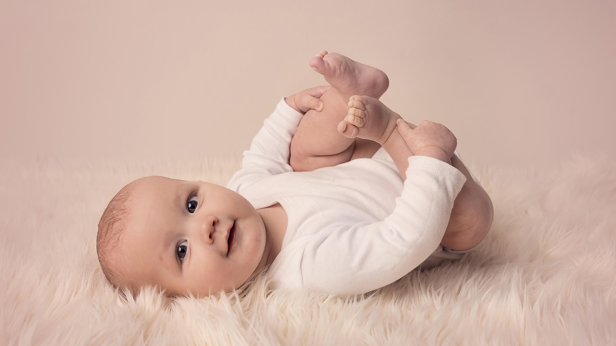 a baby laying on their back holding their toes at a photo shoot with AnA Photography in Cornwall.